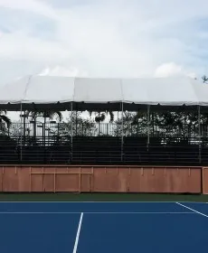 Quiet outdoor tennis court facing bleachers and clouds