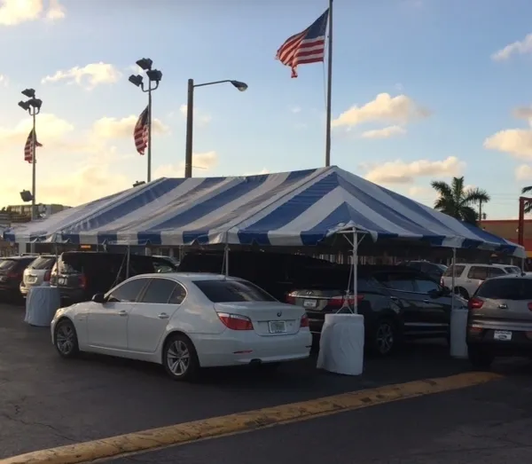 Outdoor car sale under striped tent.