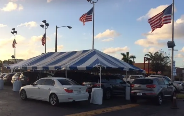White sedan beside blue-striped dealership tent