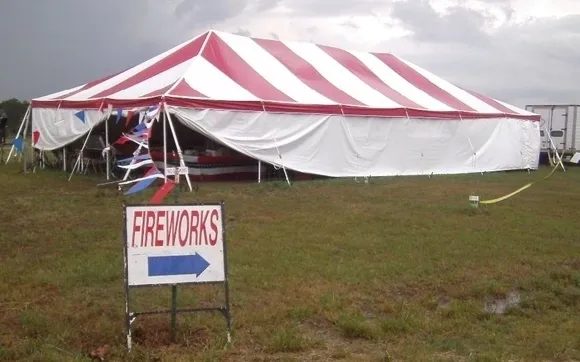 Striped tent on grassy field, fireworks sale.